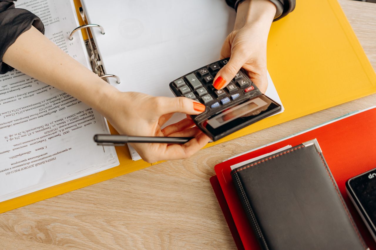 about-02 Hands using a calculator at a desk with documents and folders, ideal for finance or accounting themes.