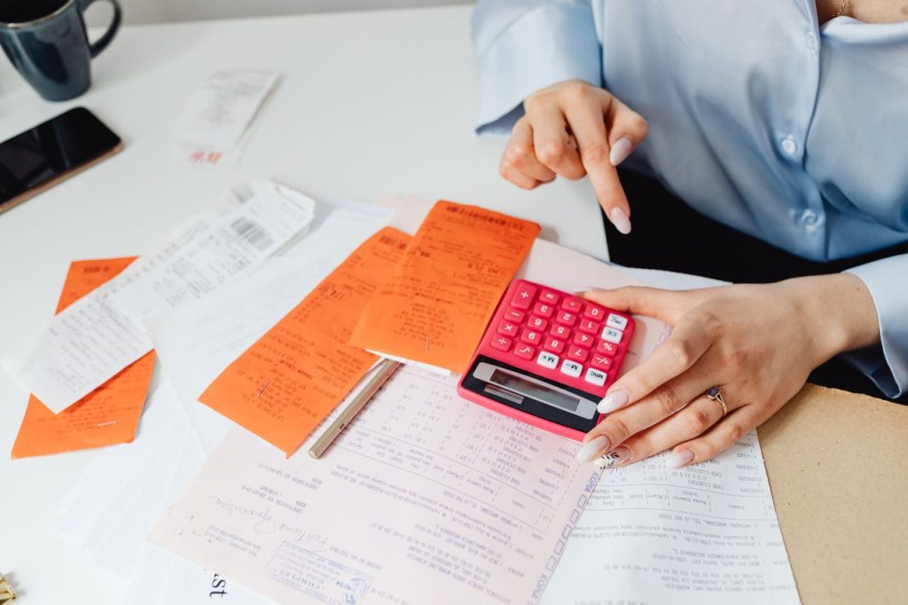 Maria Semple Bookkeeping Businesswoman calculates expenses using receipts and calculator at desk. Ideal for finance, accounting themes.
